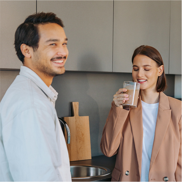 Mann und Frau stehen gemeinsam in der Küche und trinken einen Protein Shake