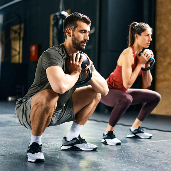 Mann und Frau machen in Fitnessraum gemeinsam Kniebeugen mit Kettlebells